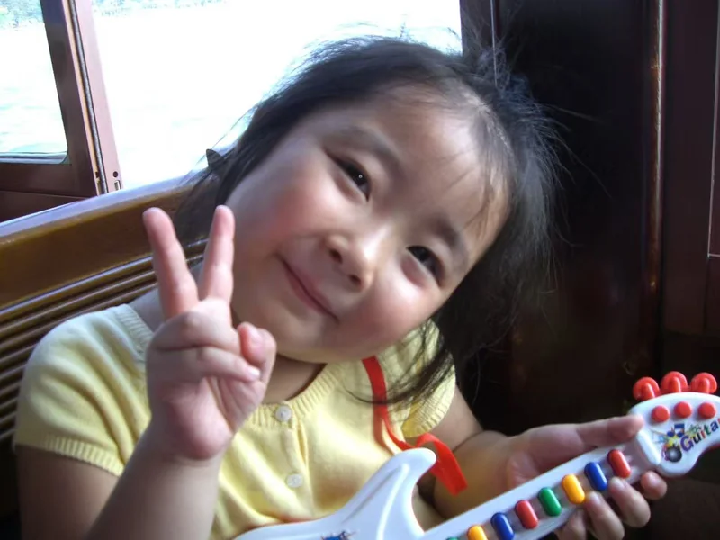 Anna as a child, holding a toy guitar and making a peace sign.